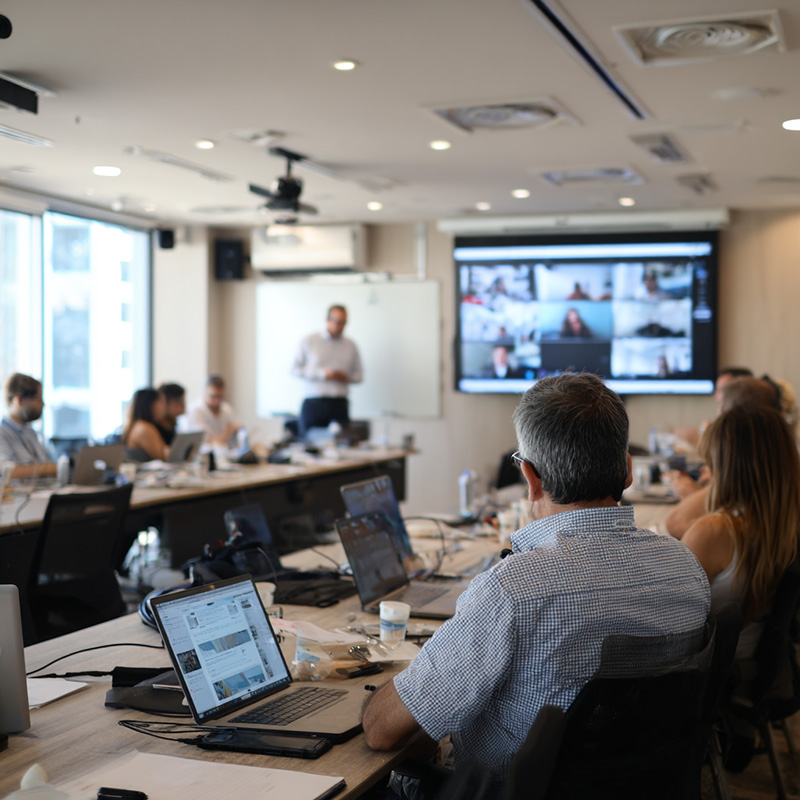 Instructor leading a hybrid training session with in-person learners and remote participants visible on a screen, illustrating flexible delivery options for corporate training.