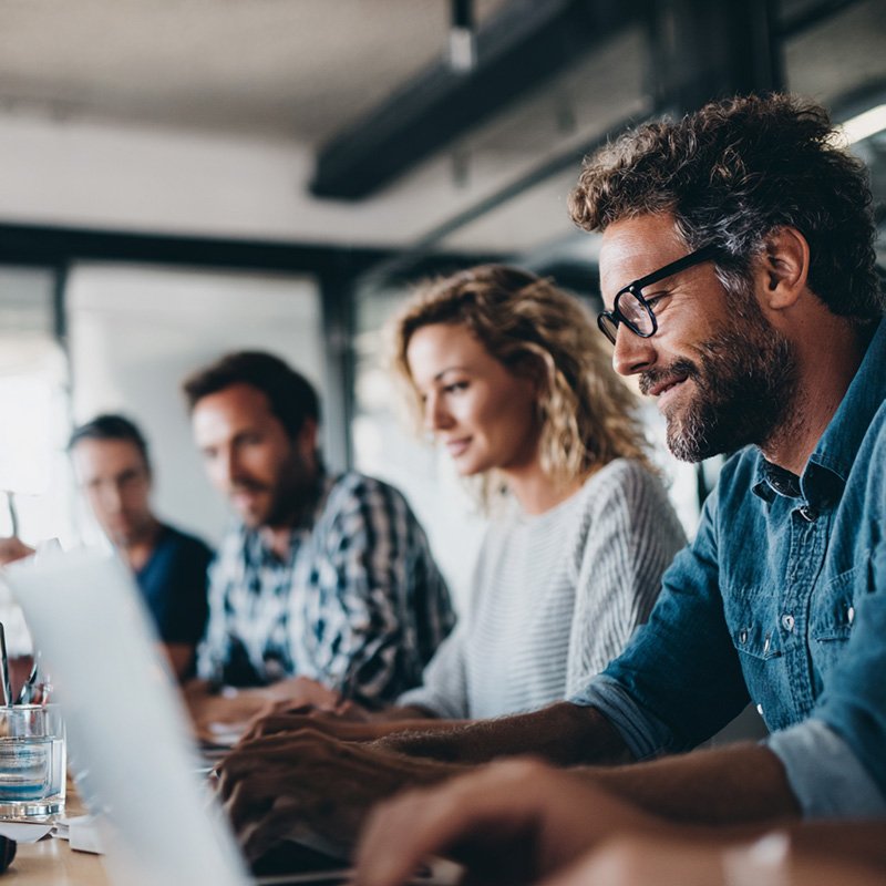 Early-career professionals collaborating with mentors in a tech training environment, with blurred screens to symbolize guided, real-world learning in an apprenticeship program.