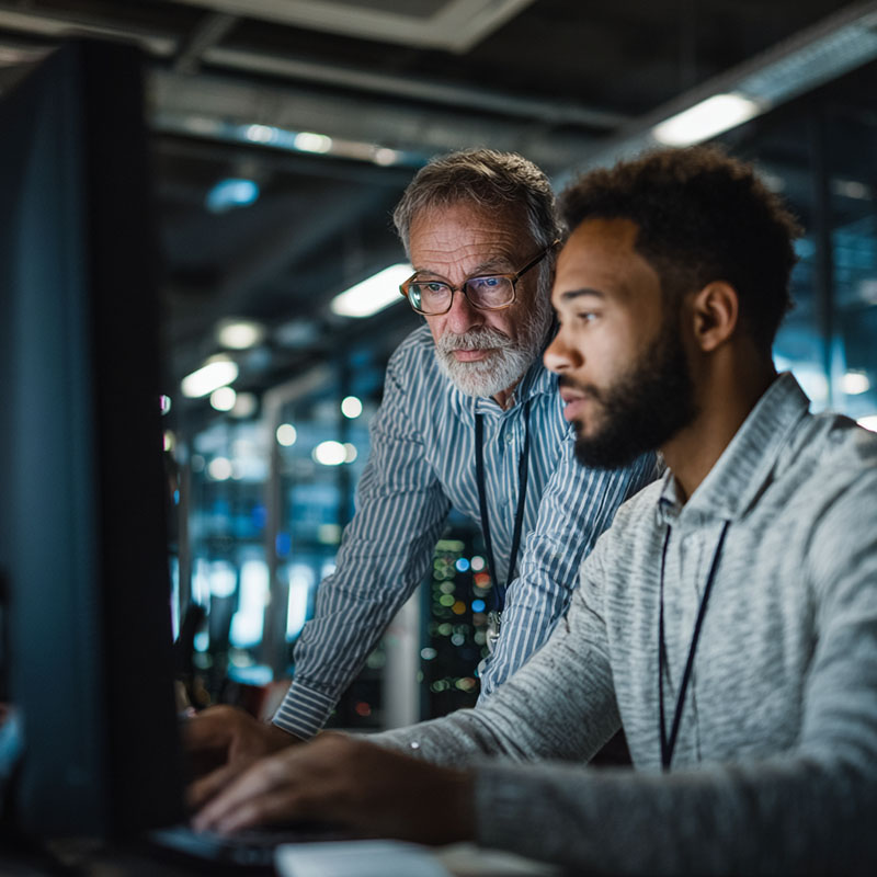 Two IT professionals from different generations collaborating in a modern enterprise environment, symbolizing mainframe skills transfer and workforce development.